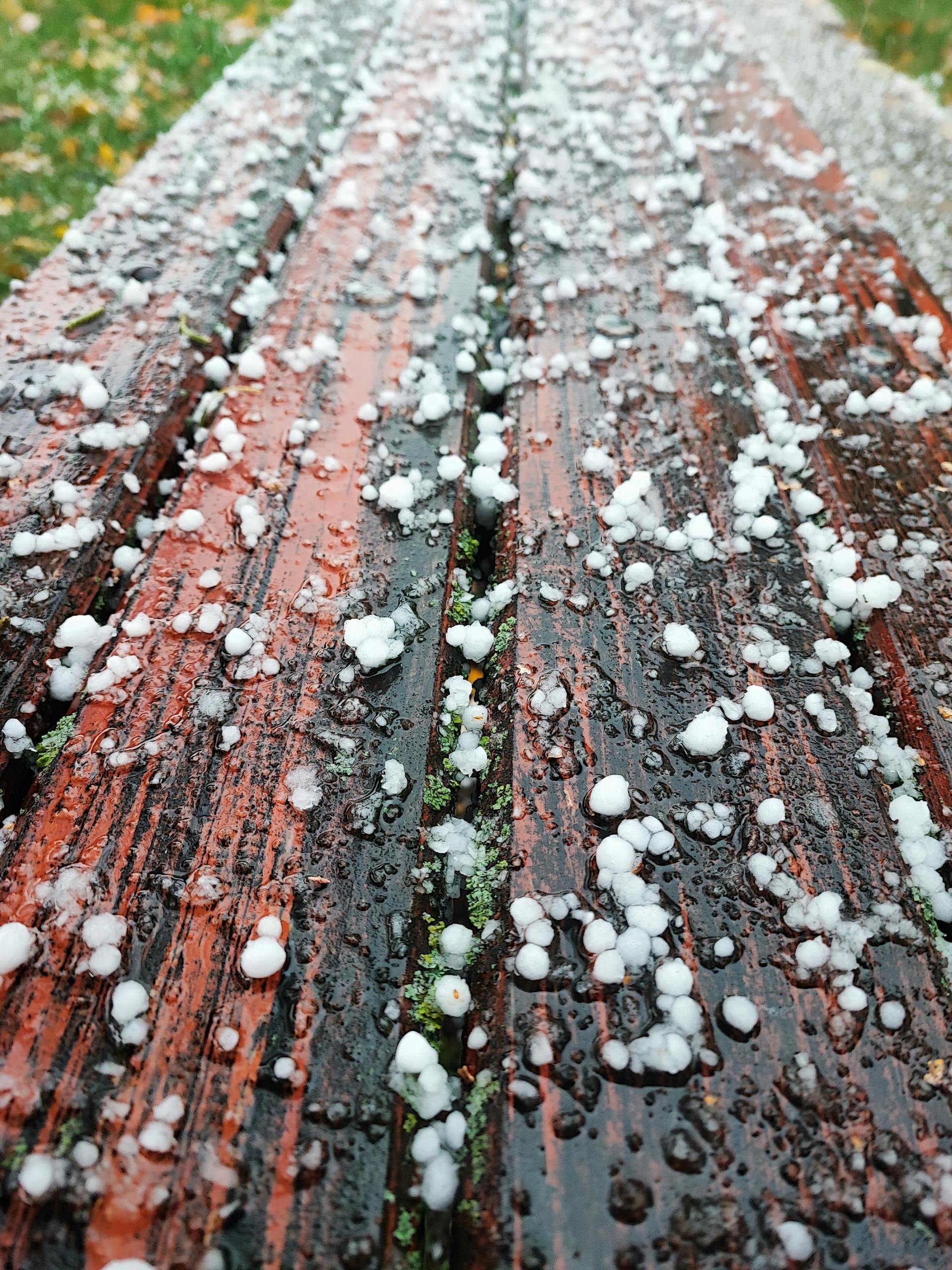 Close-up of hailstones scattered on a wet wooden surface post-storm.